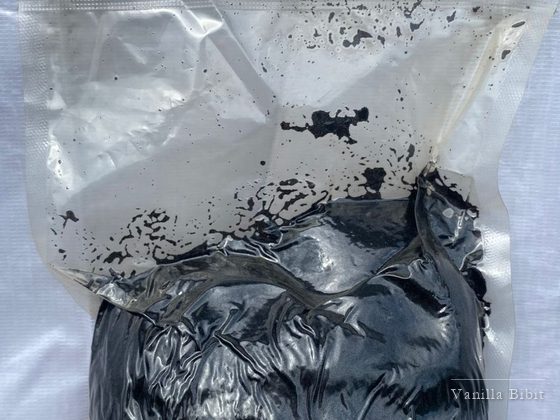 Kemasan plastik bening berisi pasta biji vanili berwarna hitam, dipegang dengan tangan.