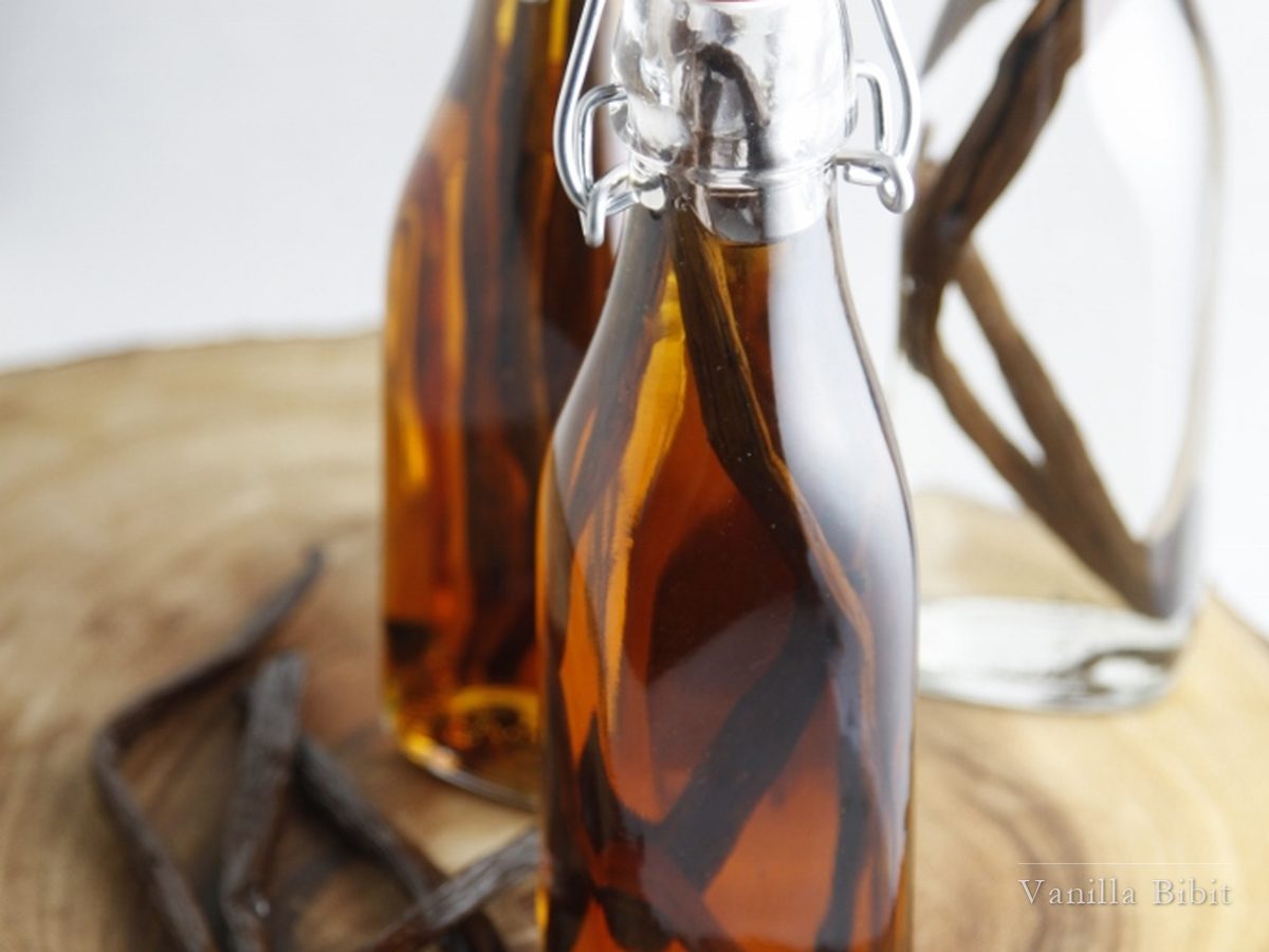 Botol kaca bertutup jepit berisi cairan cokelat keemasan dengan batang vanili di dalamnya.