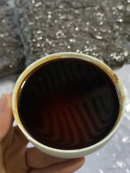 Tangan memegang kaleng terbuka berisi cairan cokelat tua.