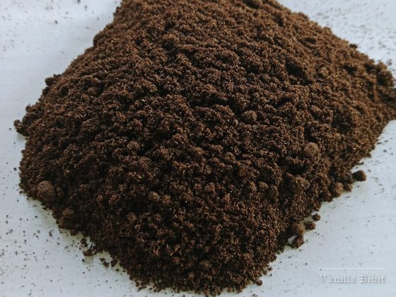 Tumpukan bubuk vanili berwarna cokelat di atas permukaan putih.