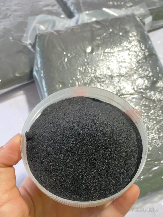 Tangan memegang kaleng terbuka berisi biji vanili hitam halus.